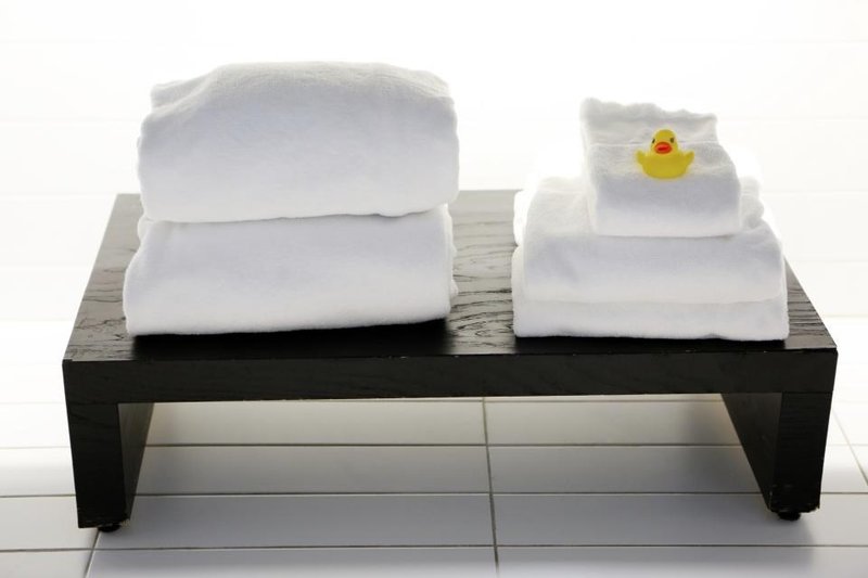 Folded white towels on a low bench beside a small yellow bath toy