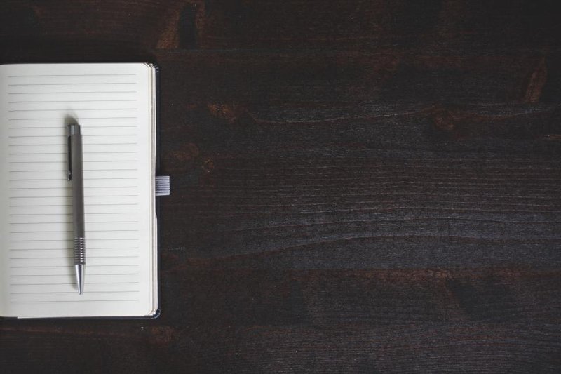 A pen resting on an open blank notebook on a dark wooden desk