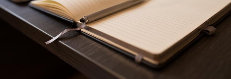 An open lined notebook and pen on a dark wooden desk