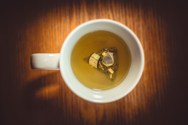 A white cup of pale tea with a tea bag on a wooden table