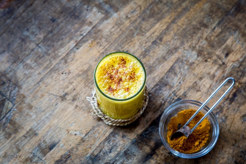 A turmeric latte beside a spoon of ground turmeric