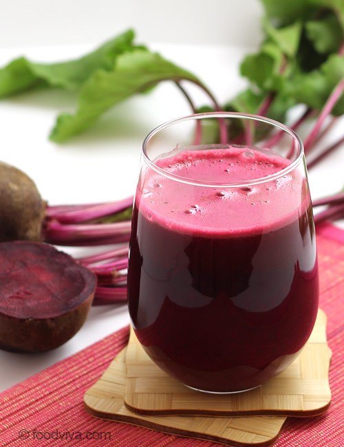 A glass of beetroot juice beside fresh beetroot and leaves