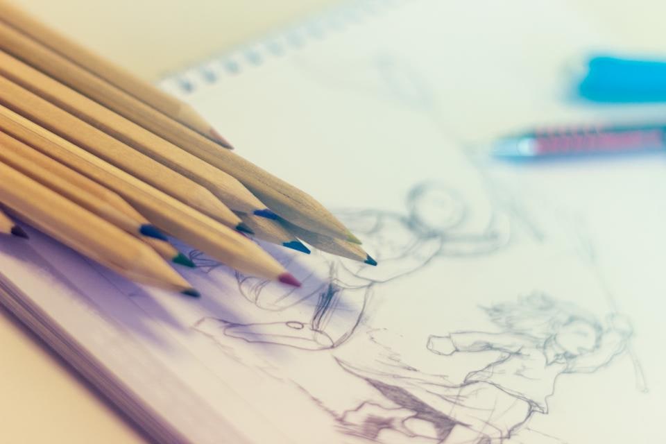 Coloured pencils beside drawings on paper