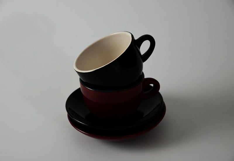 Two ceramic cups stacked with saucers on a plain surface