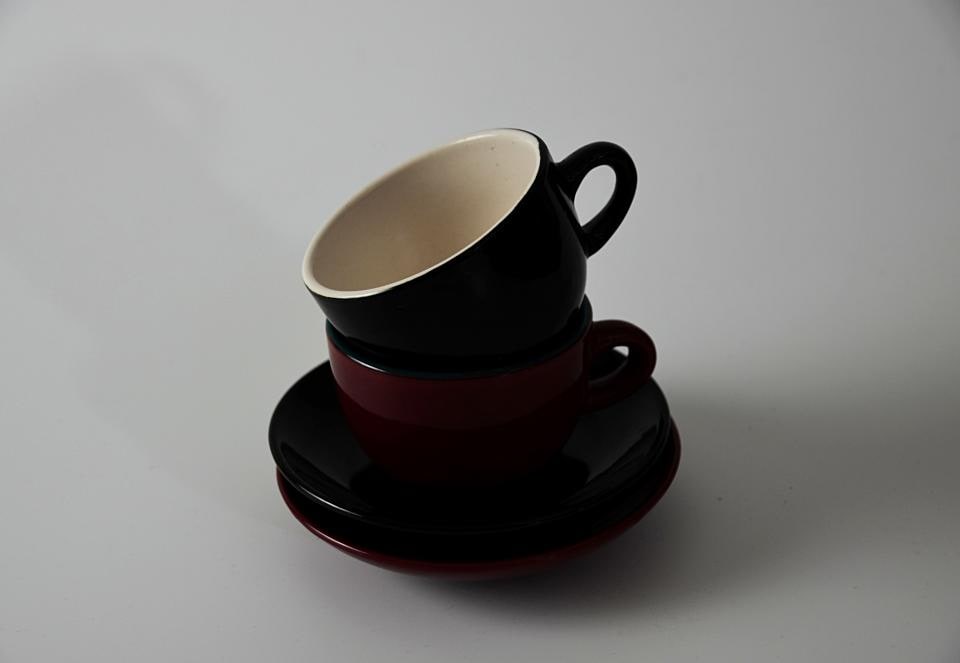 Two ceramic cups stacked with saucers on a plain surface