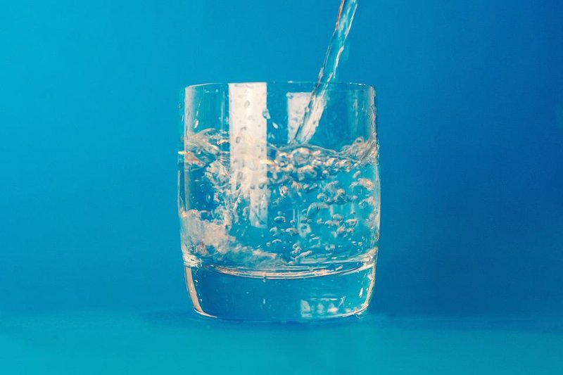 Clear water being poured into a glass against a blue background