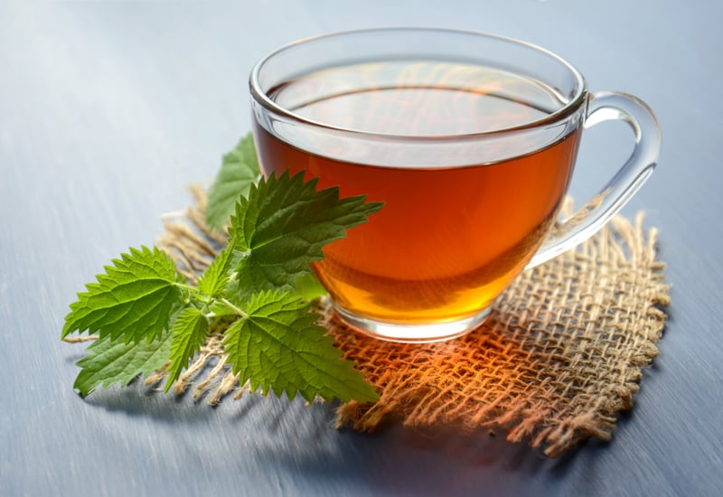 A glass cup of amber tea beside green leaves on a woven mat