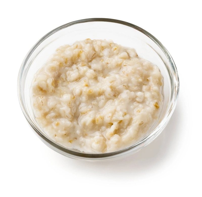 Plain cooked oats in a clear glass bowl on a white background