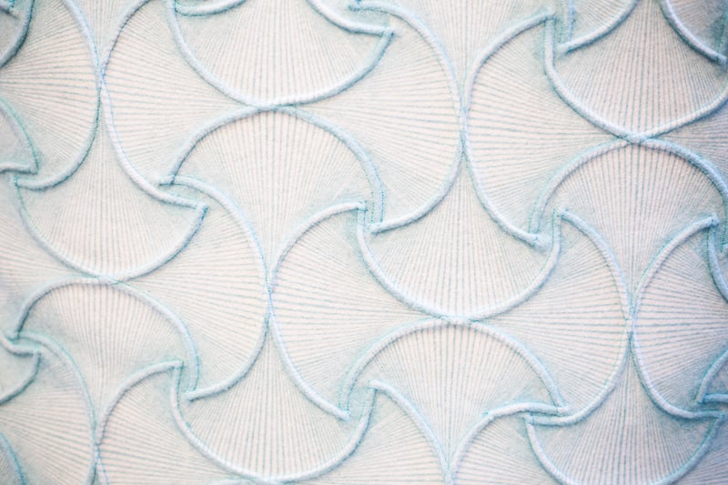 Pale woven fabric embroidered with curved blue lines