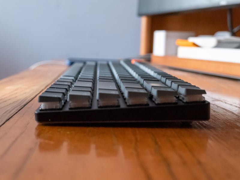 A computer keyboard on a wooden desk beside a screen