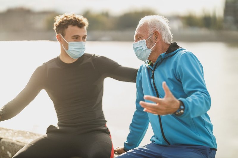 Two people wearing face masks talking together beside the water outdoors