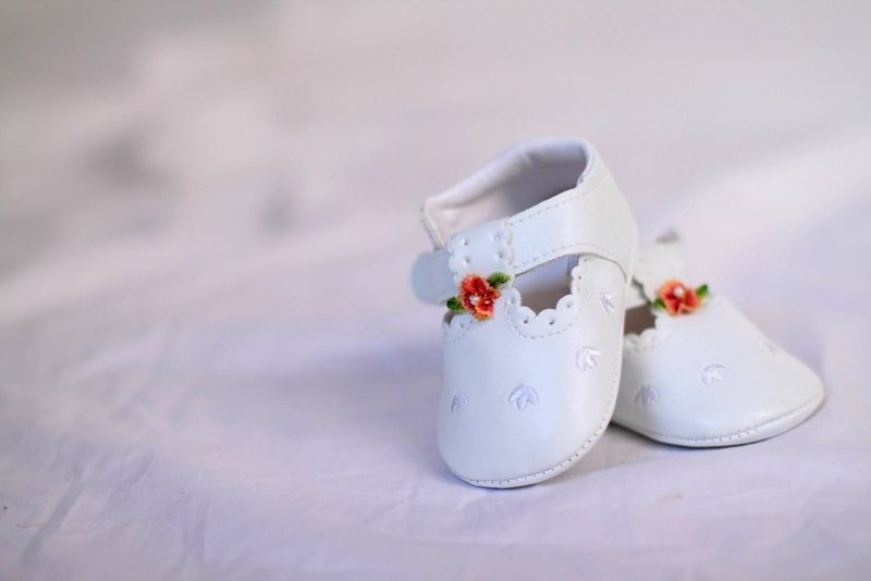 Small white baby shoes with embroidered flowers on a pale surface