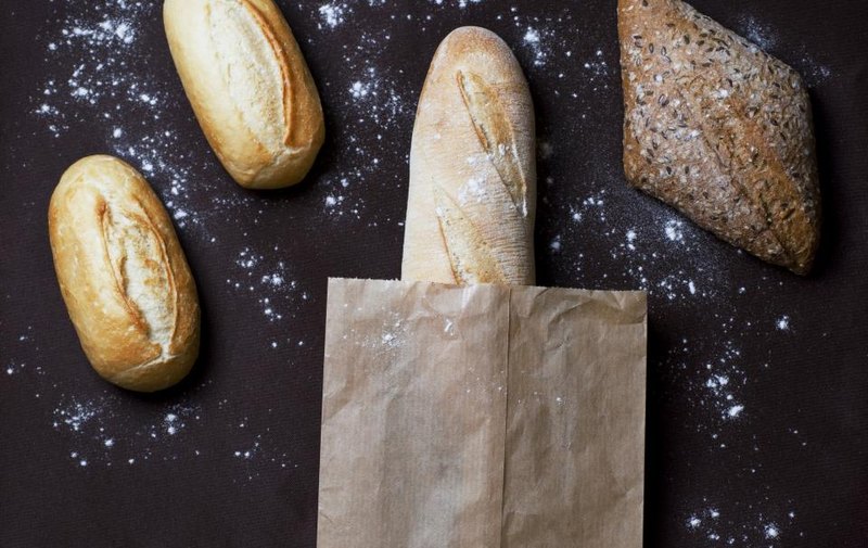 Bread rolls, a seeded loaf and a paper bag on a flour-dusted surface