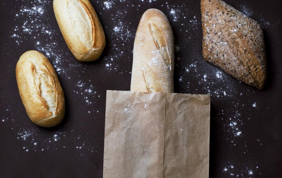 Bread rolls, a seeded loaf and a paper bag on a flour-dusted surface