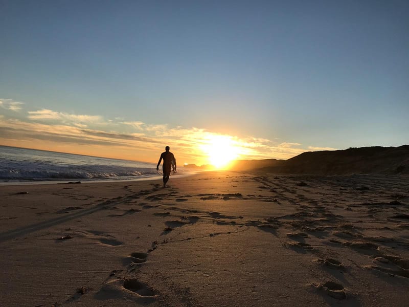 A person walking on a beach at sunset