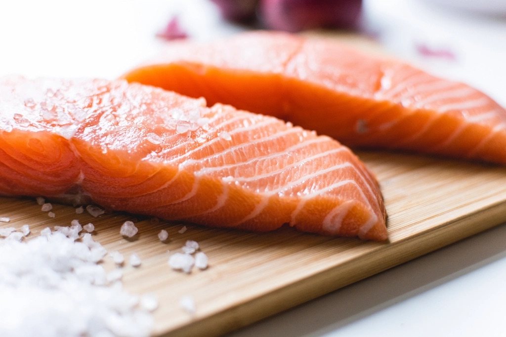 Two raw salmon fillets with coarse sea salt on a wooden chopping board