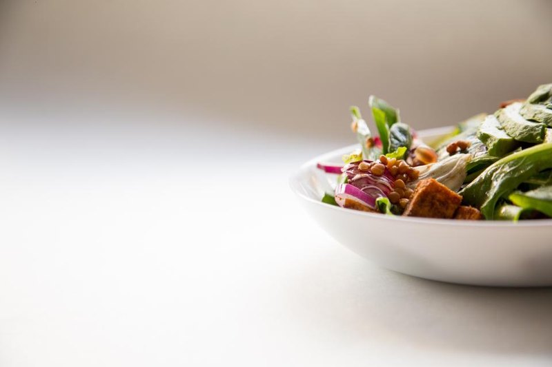 A white bowl of salad with leafy greens, cucumber and toasted bread