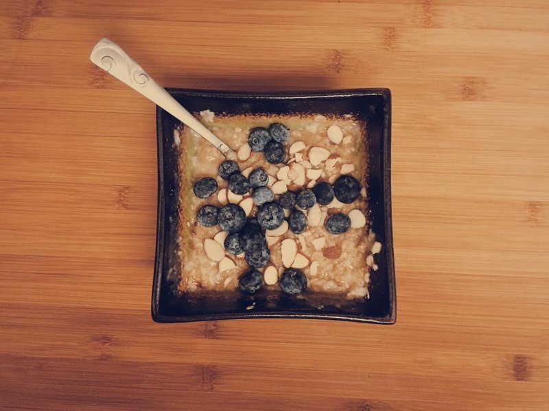 A bowl of oatmeal topped with blueberries and flaked almonds on a wooden table
