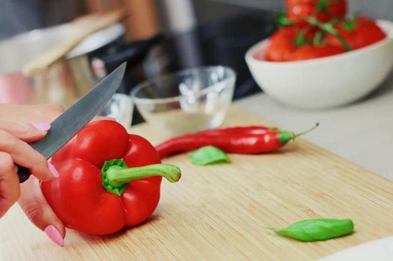 Hands cutting a red capsicum on a wooden board beside fresh vegetables