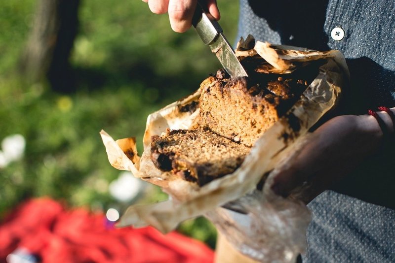 Hands slicing a rustic banana loaf outdoors