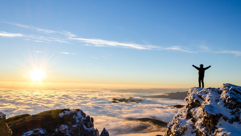 A person standing on a mountain above the clouds