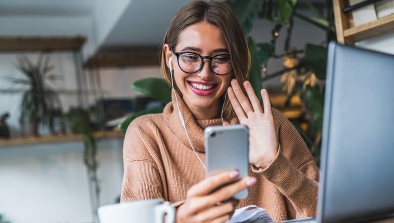 A woman smiling at her phone while holding a cup