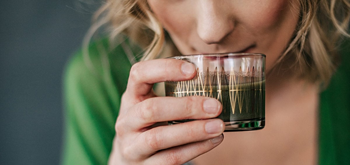 A person drinking from a glass of green juice
