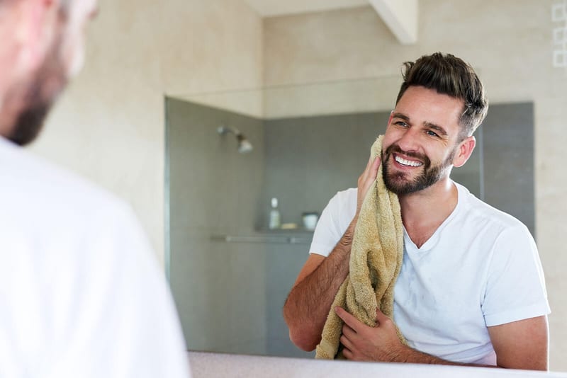 A man holding a towel against his cheek in front of a mirror