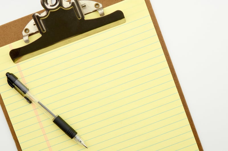 A pen on a blank yellow lined pad attached to a clipboard