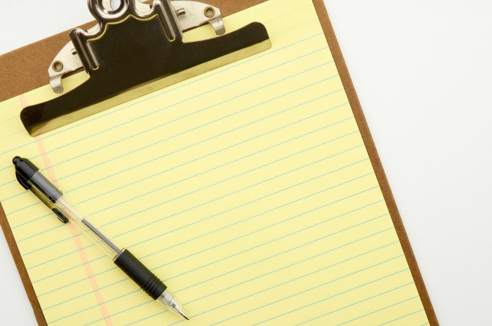 A pen on a blank yellow lined pad attached to a clipboard