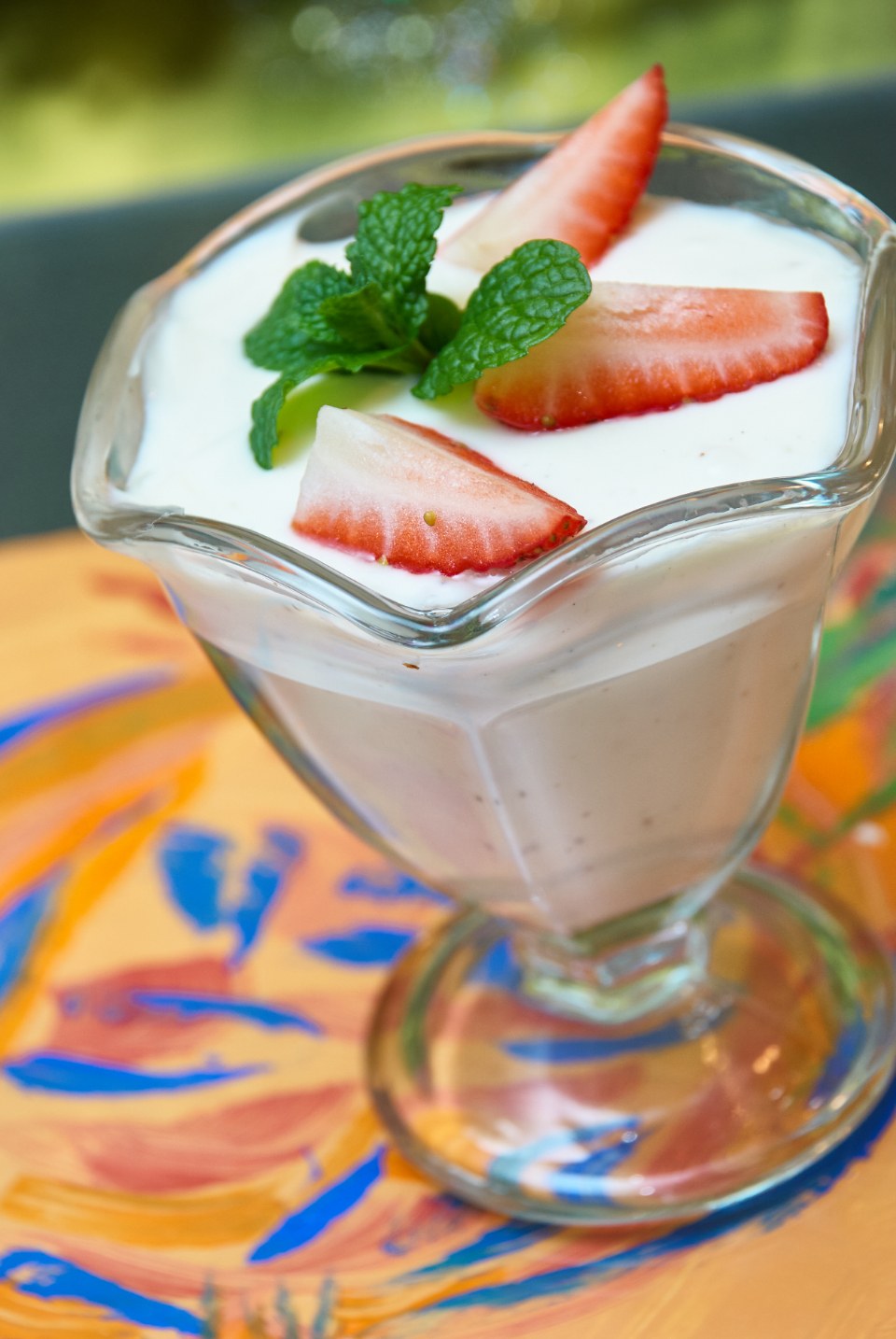 A glass of yoghurt topped with sliced strawberries and green leaves
