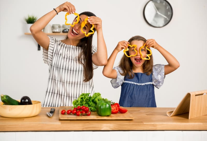 An adult and a child holding slices of capsicum while preparing vegetables