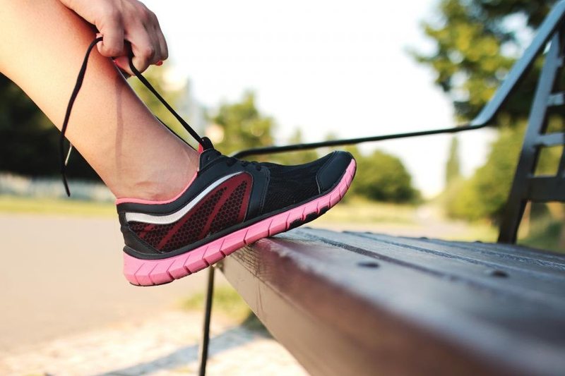 A person tying a black and pink running shoe on an outdoor bench