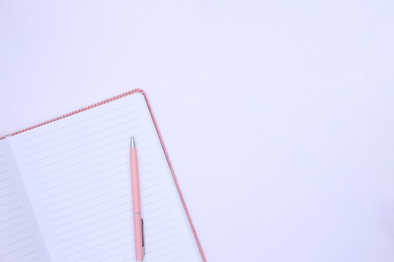 An open lined notebook and pink pen on a pale surface