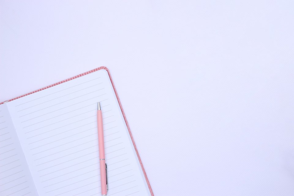 An open lined notebook and pink pen on a pale surface