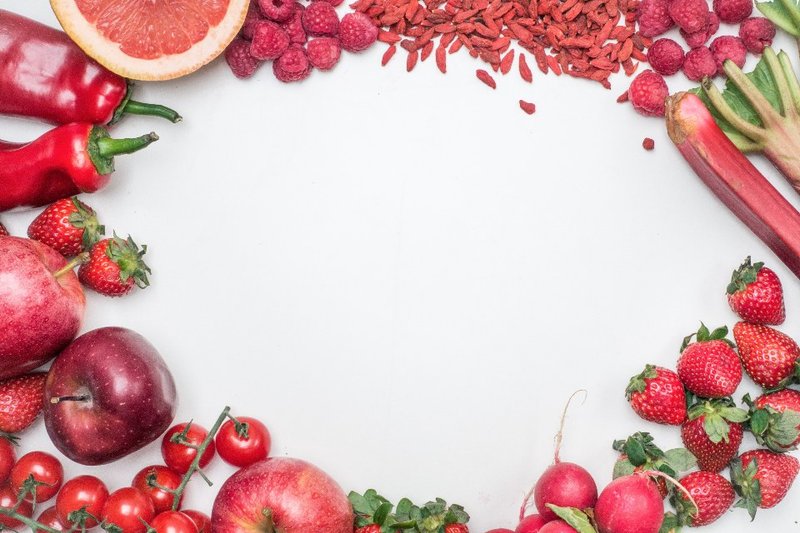 Red fruit and vegetables arranged around a white background