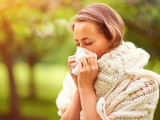 A person wearing a scarf and holding a tissue to their nose outdoors