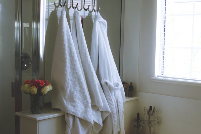 White towels and a robe hanging beside a bathroom window and a vase of flowers