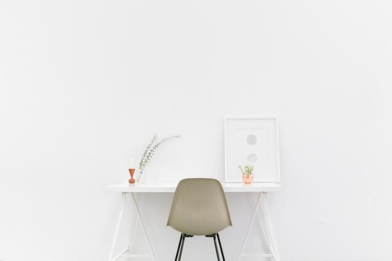A simple white desk and chair with a small plant against a pale wall