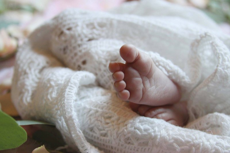 A newborn baby’s foot resting against a soft white knitted blanket