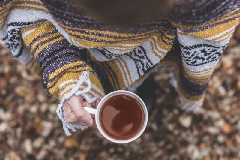 A hand holding a mug of tea beside a patterned woollen jumper