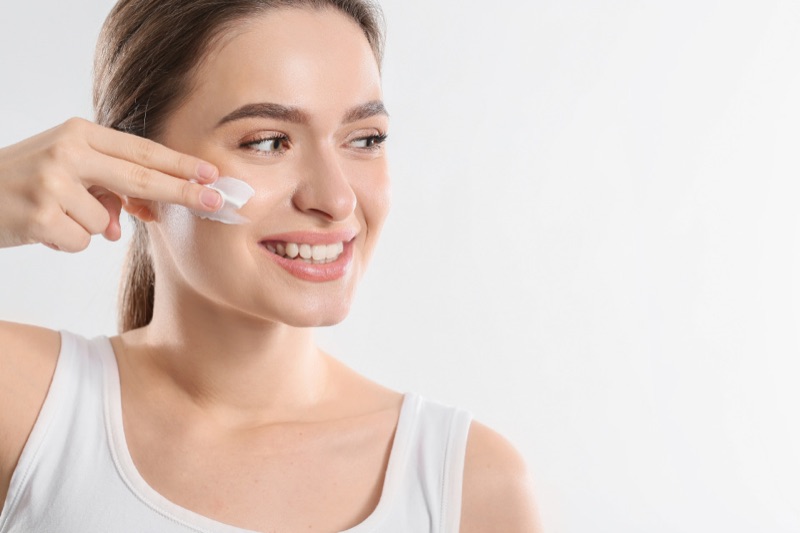 A woman gently applying cream to her cheek