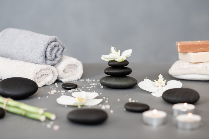 Folded towels, smooth stones and white flowers arranged on a grey surface