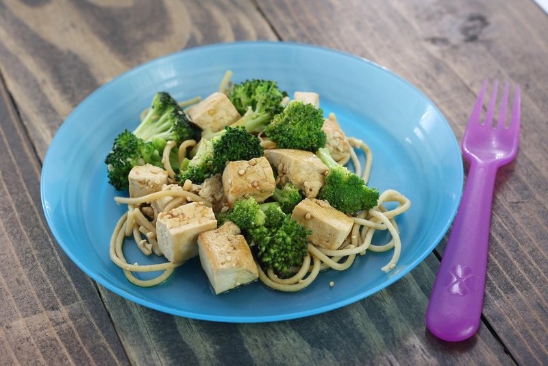 Tofu, broccoli and noodles on a blue plate beside a purple fork