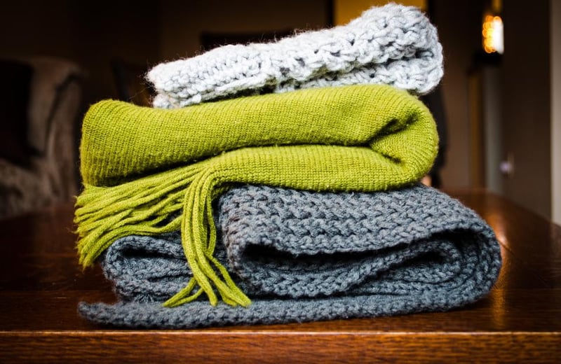 Folded grey knitted blankets with a green scarf on a wooden table
