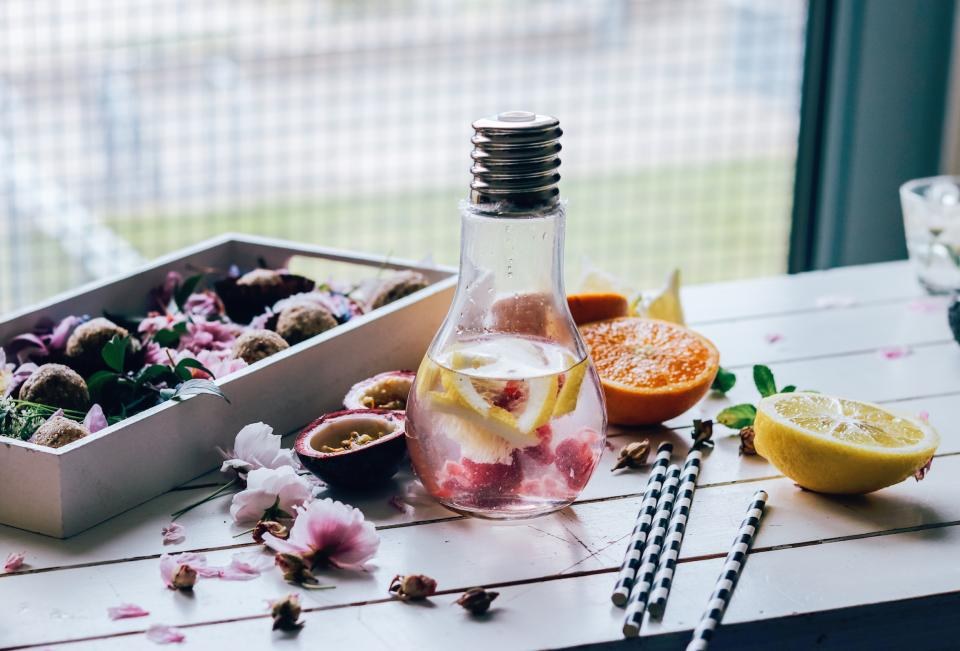 Water with citrus and flower petals in a clear bottle beside cut citrus fruit