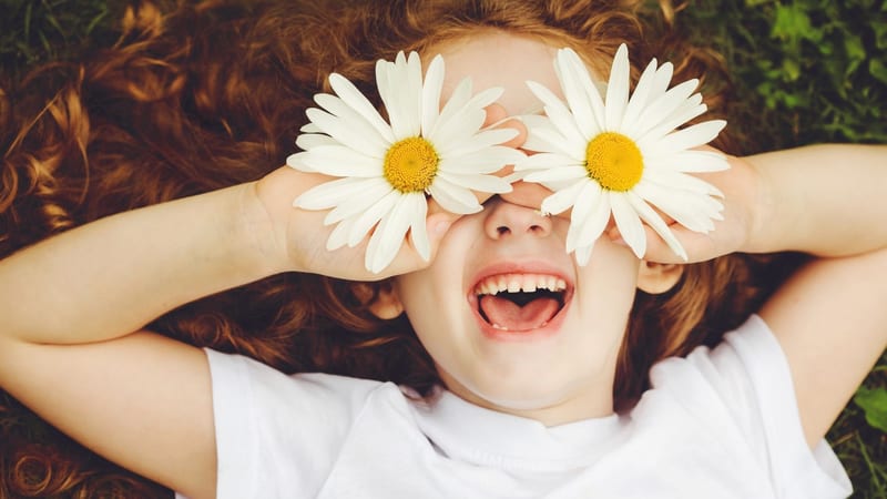 A child holding daisies over their eyes