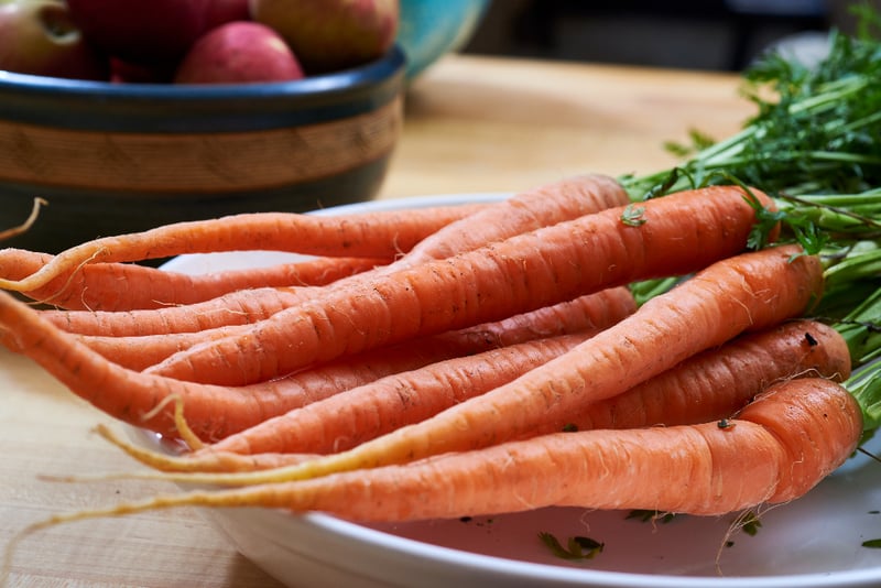Fresh carrots with leafy tops on a wooden chopping board