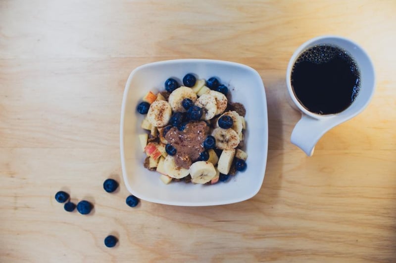 A breakfast bowl with banana slices and blueberries beside a cup