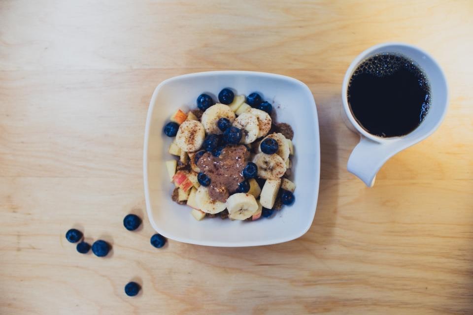 A breakfast bowl with banana slices and blueberries beside a cup